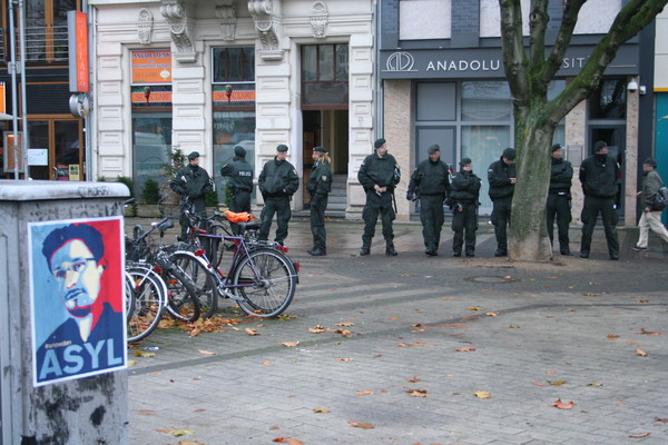 [Foto: Asyl-fr-Snowden-Plakat mit Polizei-Reihe im Hintergrund]