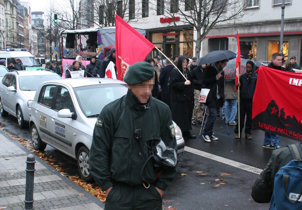 [Foto: Polizist mit Kamera neben Demo-Zug]