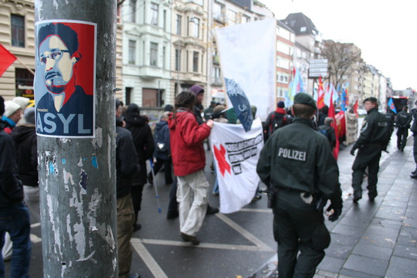 [Foto: Asyl-fr-Snowden-Aufkleber mit Demo-Zug im Hintergrund]