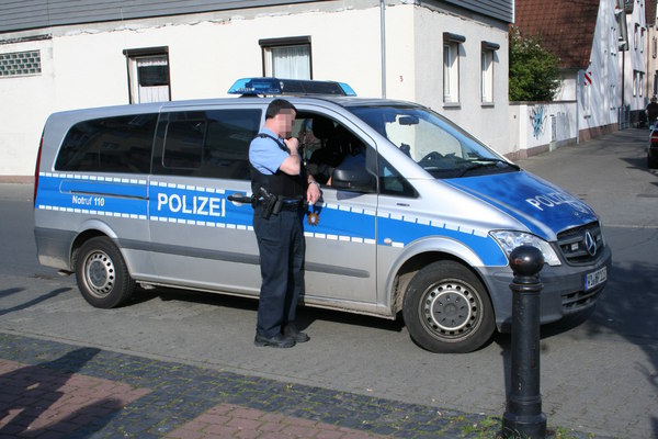[Foto: Funkender Polizist vor Polizei-Bus]