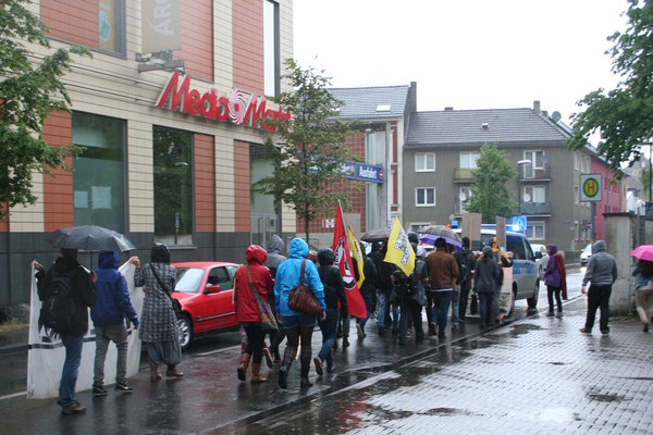 [Foto: Demonstranten passieren Media-Markt im Regen]